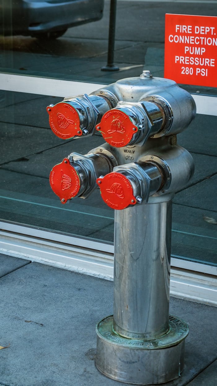 Vertical shot of an urban fire hydrant with red connection caps on a city sidewalk.